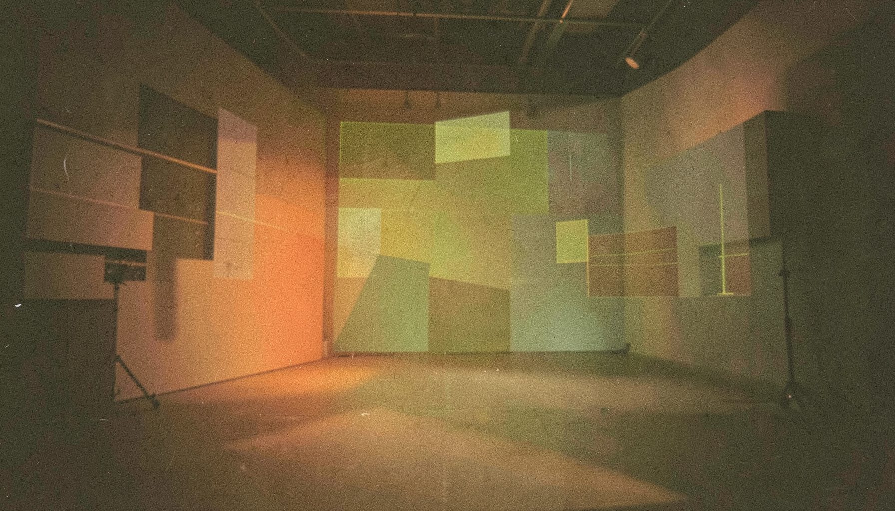 A grainy analog film still of a softly lit studio space with warm amber and olive tones, abstract geometric shapes suggesting a creative digital workspace.